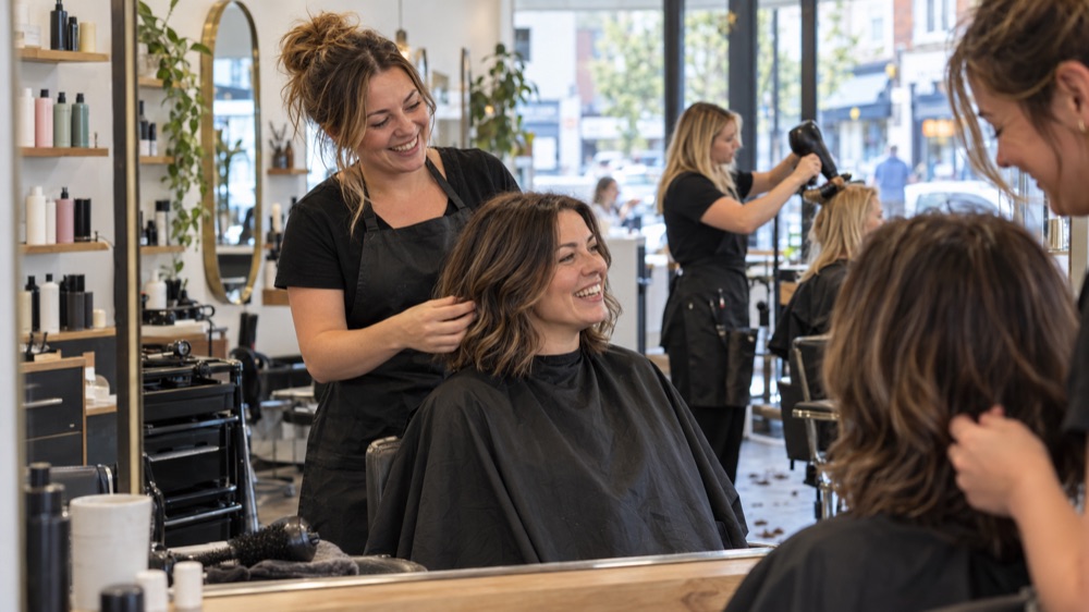 Hairdresser styling a smiling client's hair in a bright salon